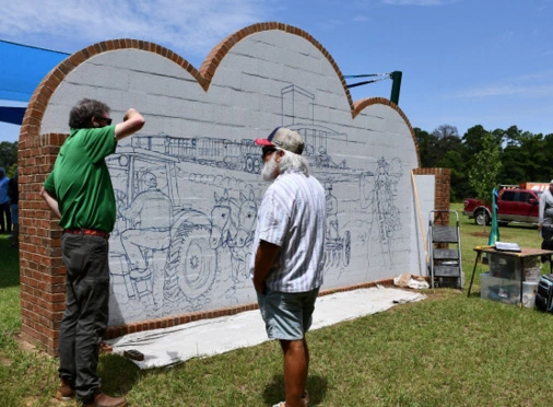 Hare, right, talks with an attendee of the Chapel in the Oaks ribbon cutting. His large mural on the back side of the altar wall is his “love letter” to the Wiregrass.
