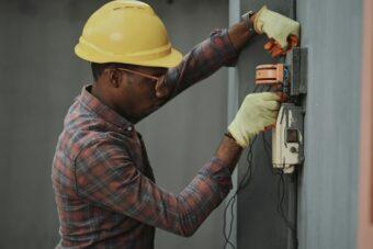 A man in a hard hat and safety glasses is diligently working on an electrical box, ensuring safety and efficiency.