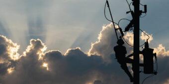A man is climbing a telephone pole, working on electrical lines high above the ground.